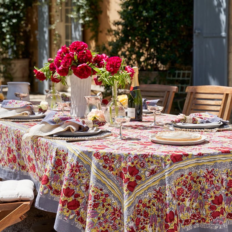 Caravan Home 71 x 71 Red & Grey Tablecloth with a vibrant floral design, elegantly draped on a table, featuring a vase of flowers as a centerpiece.