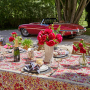Caravan Home | 71 x 71 Red & Grey Tablecloth elegantly drapes a table adorned with plates, glasses, and a floral centerpiece, reflecting French-inspired craftsmanship.