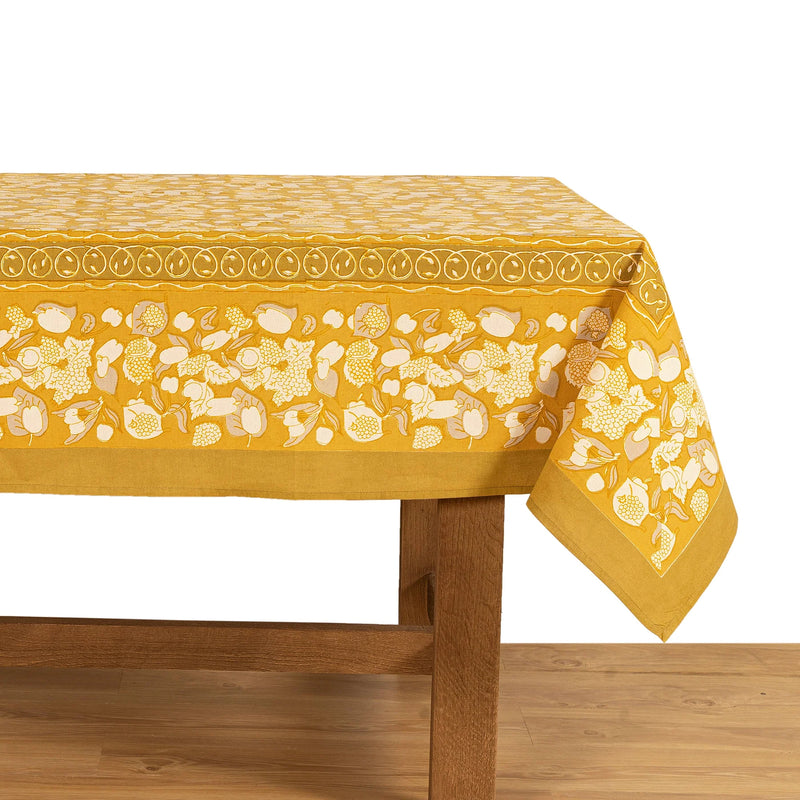 Forest Harvest Grey & Mustard Tablecloth features hand-printed fruit and foliage design on a wooden table, ideal for enhancing dining settings with artisanal craftsmanship.