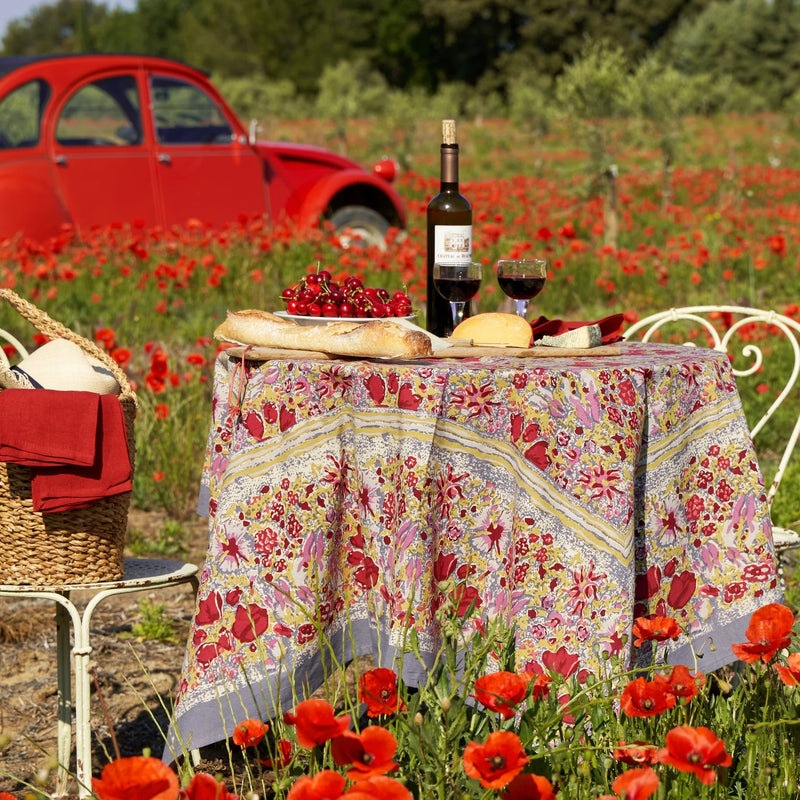Caravan Home 71 x 71 Red & Grey Tablecloth elegantly draped on a floral-themed outdoor table, set amidst a field of flowers with wine and picnic items.