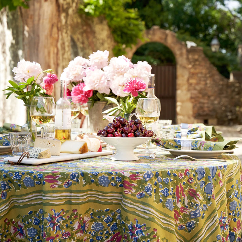 Jardin Blue & Vert Tablecloth by Caravan Home on a table set with cherries and flowers, showcasing handprinted craftsmanship inspired by Southern France gardens.