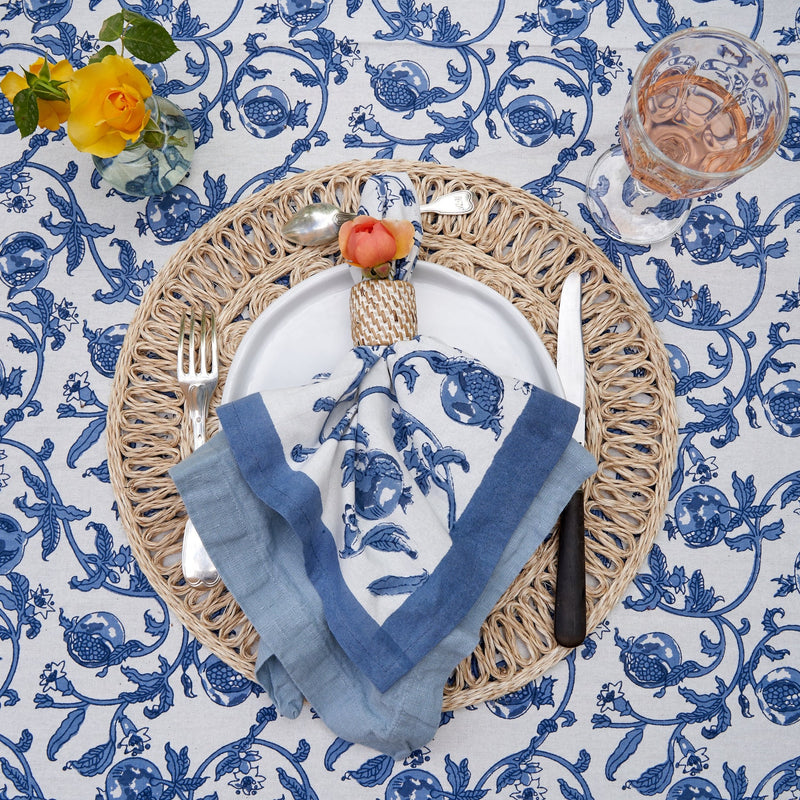 Granada Cornflower Blue Napkins Set of 6, featuring intricate floral and pomegranate design, elegantly set on a table with a yellow rose centerpiece.