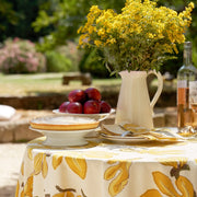 Caravan Home Fig Citrine Tablecloth on a table with flowers and pie, showcasing its handprinted design, perfect for elegant dining settings.