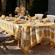 Table set with food and wine on a 71 x 71 Fig Citrine Tablecloth by Caravan Home, ideal for elegant dining experiences.
