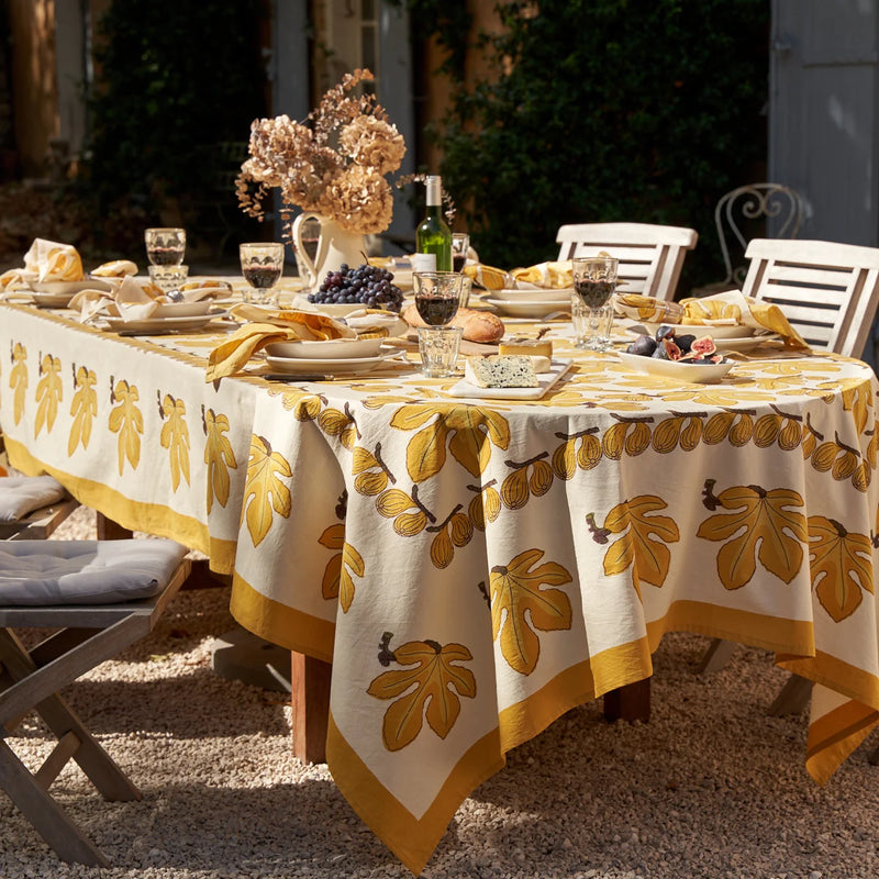 Caravan Home Fig Citrine Tablecloth on a set dining table with food, wine, and flowers, highlighting its elegant handprinted design for special occasions.