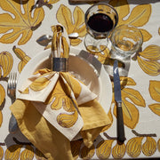 Caravan Home | 59 x 86 Fig Citrine Tablecloth elegantly drapes a table, accompanied by tableware and wine glasses, showcasing handprinted French linen craftsmanship for a refined dining setup.