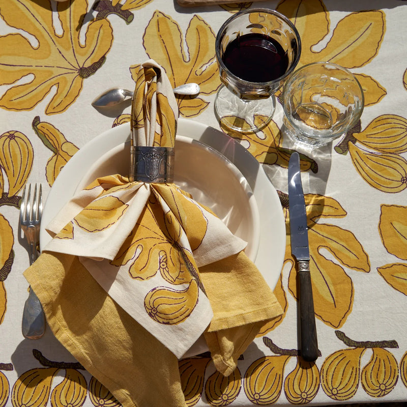 Caravan Home 71 x 71 Fig Citrine Tablecloth elegantly displayed with tableware, including a knife and fork, on a refined dining setup.