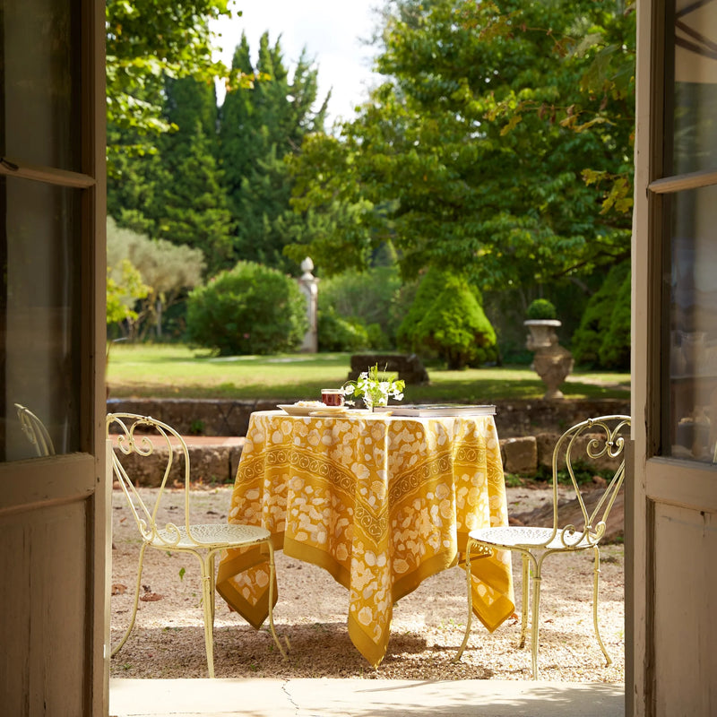 Caravan Home 71 x 71 Forest Harvest Grey & Mustard Tablecloth on outdoor table, featuring hand-printed fruit and foliage design, enhancing dining ambiance.