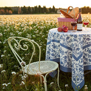Granada Cornflower Blue Tablecloth on a picnic table in a field, complemented by wine, apples, and a picnic basket.