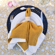 Caravan Home | 21 x 21 Dijon Everyday Napkins Set of 4, elegantly folded on a plate, showcasing their oversized, hand-dyed linen texture and mitered corners.
