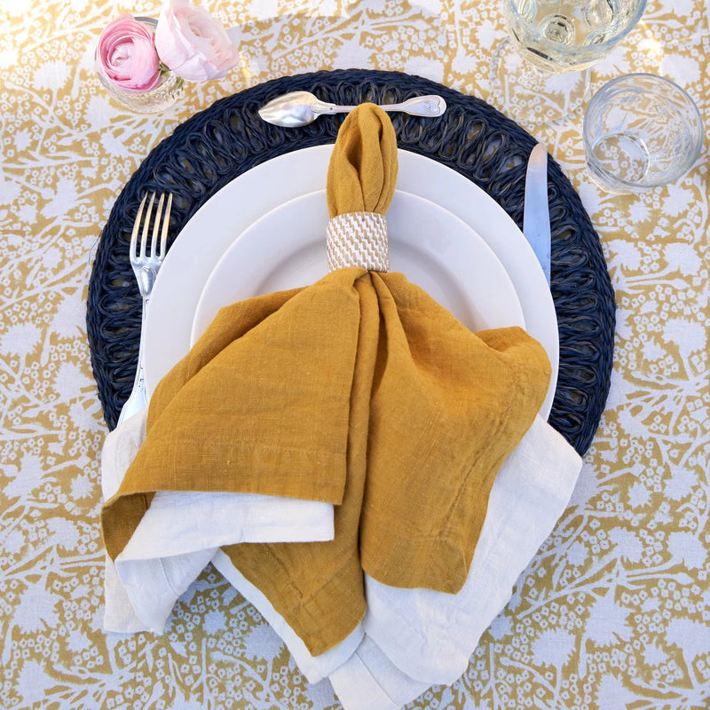 Caravan Home | 21 x 21 Dijon Everyday Napkins Set of 4, elegantly folded on a plate, showcasing their oversized, hand-dyed linen texture and mitered corners.