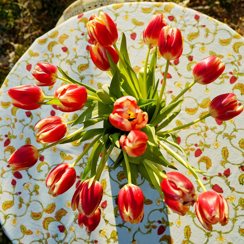 Caravan Home 71 x 106 Fraises des Bois Blue Tablecloth, adorned with red tulip bouquet, showcasing artisan handprinted craftsmanship for an elegant table setting.