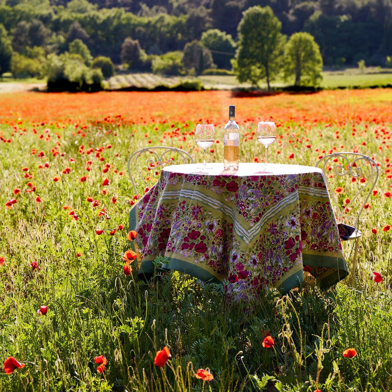 Caravan Home | 59 x 86 Red & Green Tablecloth elegantly draped on a table amidst a field of flowers, showcasing its handprinted, French-inspired design.
