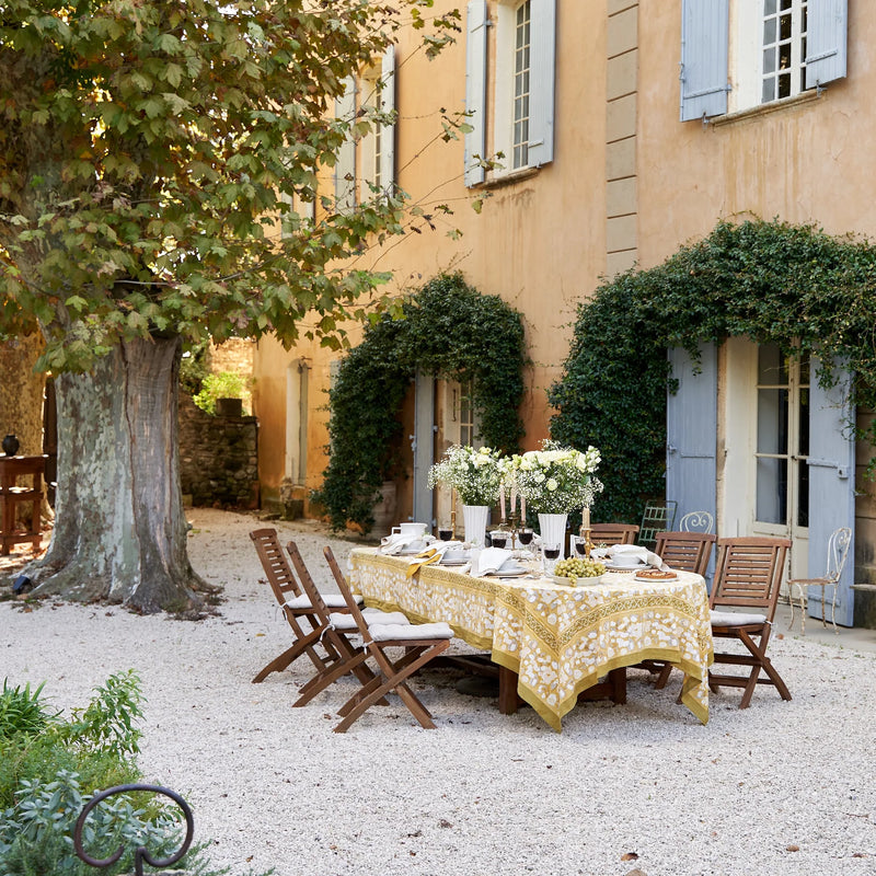 Caravan Home's 59 x 86 Forest Harvest Grey & Mustard Tablecloth elegantly drapes an outdoor table, showcasing artisanal craftsmanship with intricate fruit and vine patterns.