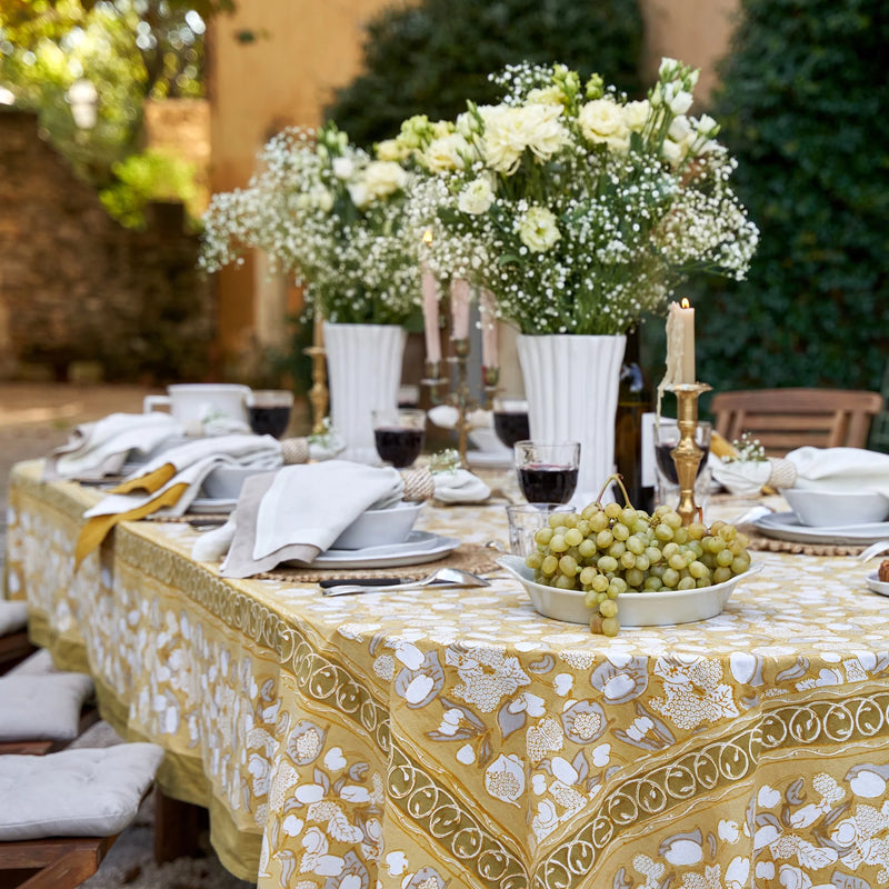 Caravan Home | 71 x 106 Forest Harvest Grey & Mustard Tablecloth, adorned with hand-printed fruit and foliage, set elegantly on a table with grapes and flowers.