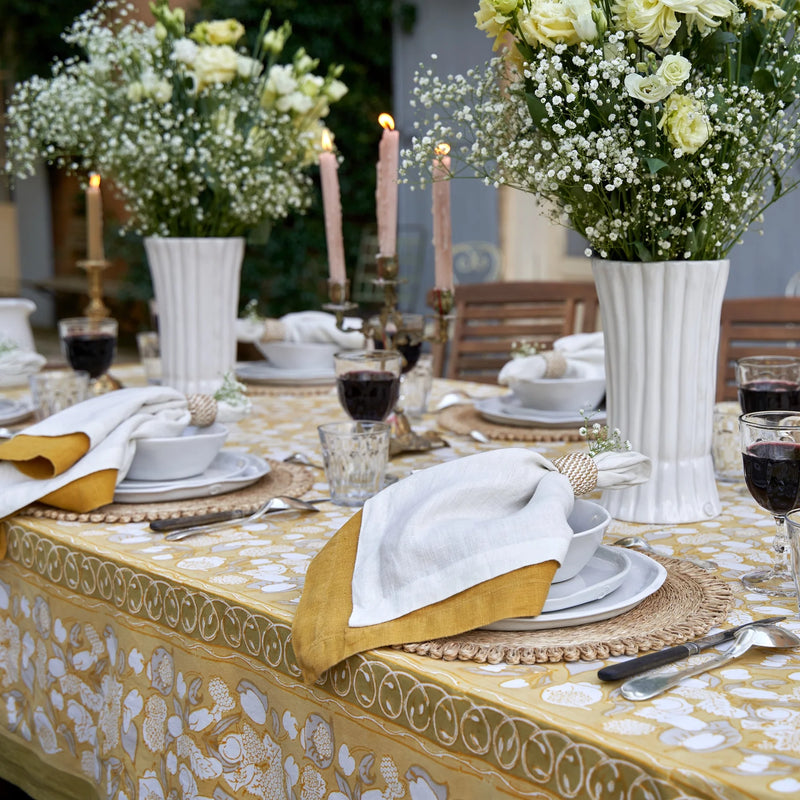 Caravan Home | 21 x 21 Dijon Everyday Napkins Set of 4 elegantly arranged on a dining table with a white vase, flowers, and wine glasses.