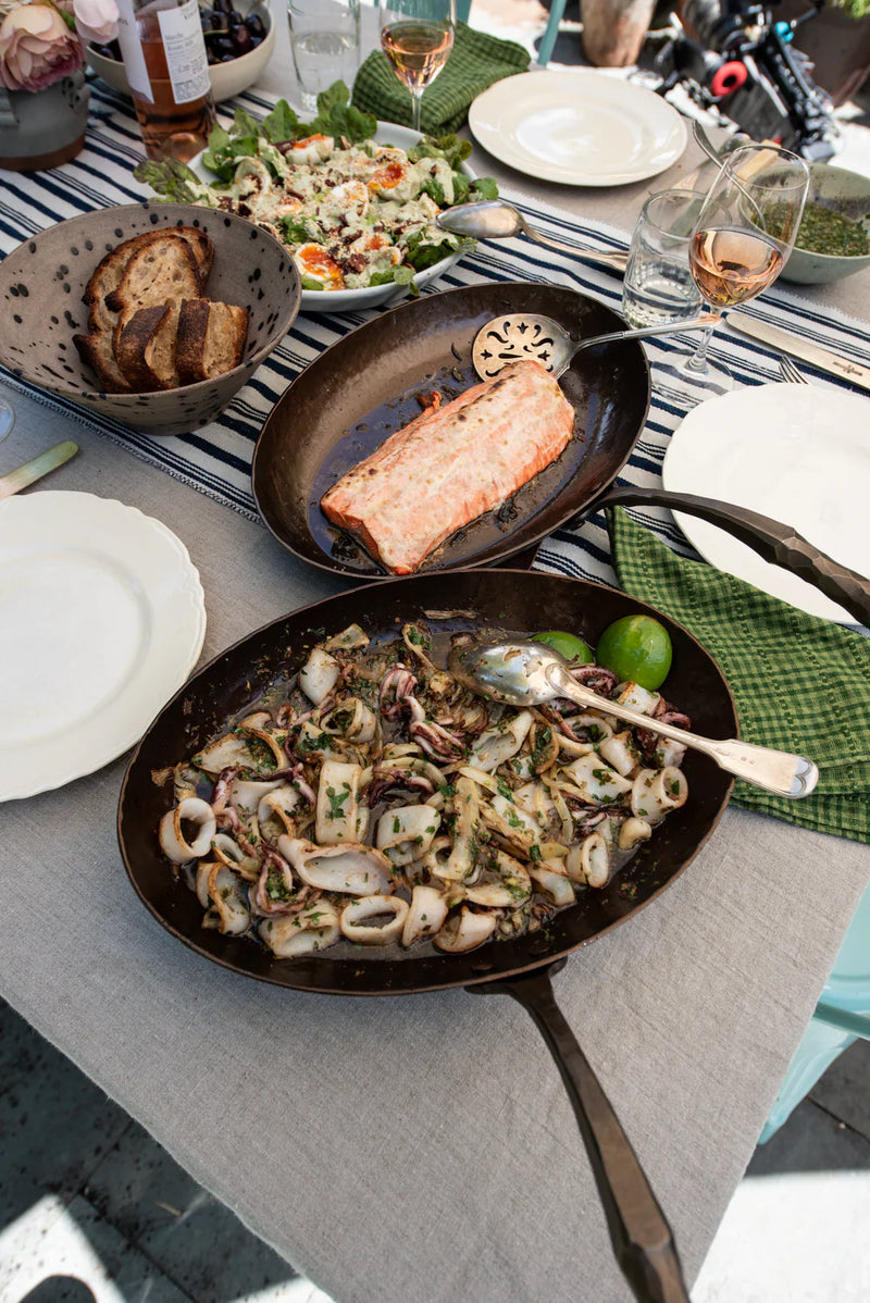 Smithey | The Fish Skillet with sautéed calamari and herbs, part of an al-fresco meal setting, showcasing its versatility for culinary creations.