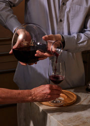 Holcomb Studio | Birdie Wine Decanter: A person elegantly pouring wine into a glass, showcasing the decanter's aerating sphere and minimalist ash wood trivet base.