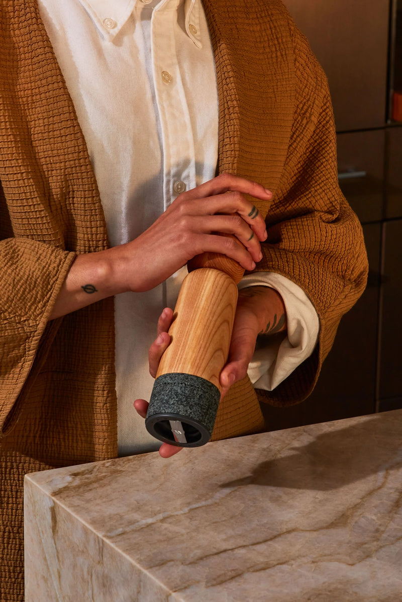 Hand holding Holcomb Studio Stone Pepper Mill, showcasing its sleek wooden design, offered by Athens Cooks kitchen store.