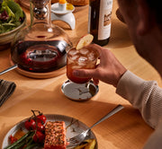 Holcomb Studio Puddle Coasters, Set of Four, sleek stainless steel design with anti-slip pads, held by a person, ideal for protecting surfaces from condensation and spills.