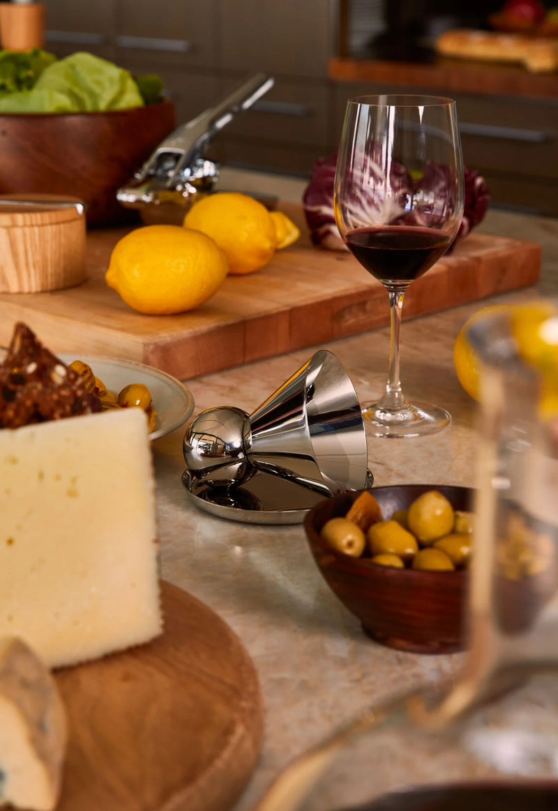 Holcomb Studio | Birdie Wine Decanter showcasing its hand-blown glass design on a counter, highlighting its aerating sphere and ash wood trivet.