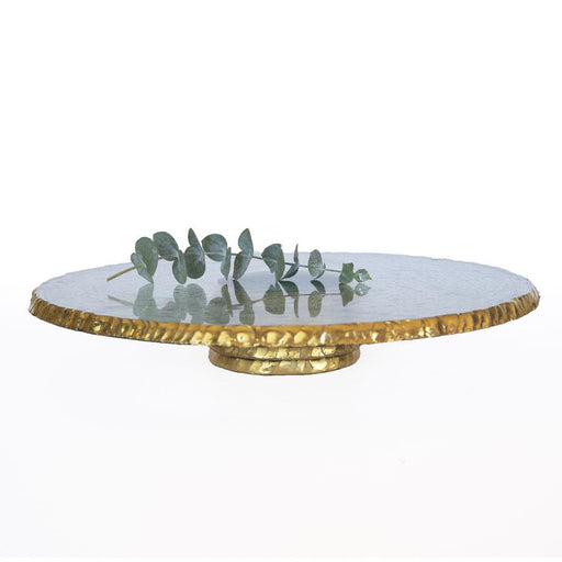 Annie Glass | Edgey Cake Stand features a hammered-gold rim and base, topped with a eucalyptus branch, showcasing its elegant, hand-chipped 24k gold-edged glass plate.