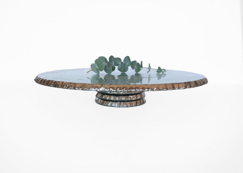 Annie Glass | Edgey Cake Stand featuring a textured bronze base and smooth top, adorned with a eucalyptus stem, showcasing its elegant, hand-chipped design.