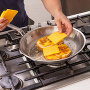 Heritage Steel | Eater Fry Pan - 8.5 Inches on a gas range, assembling grilled cheese with sautéed onions and cheddar, showcasing its even heat distribution and durability.