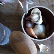 Emile Henry | Garlic Pot, Truffle: A ceramic bowl with lid, holding garlic heads and a shallot, designed for optimal storage with vent openings.