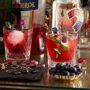 Joanna Buchanan Party Set featuring cocktail picks and wine charms alongside glasses of red cocktails and blueberries, ideal for enhancing your entertaining experience.