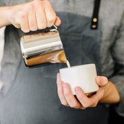 FELLOW | Eddy Steaming Pitcher, 12 oz., used to pour frothy milk into a ceramic cup, ideal for crafting precise latte art.