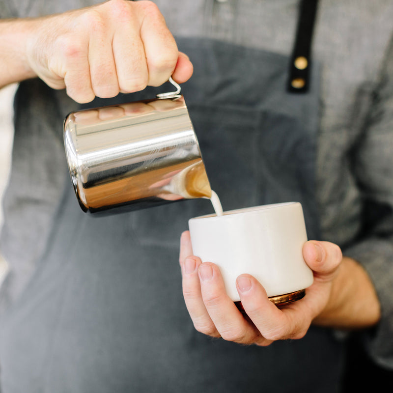 FELLOW | Eddy Steaming Pitcher, 12 oz., used to pour frothy milk into a ceramic cup, ideal for crafting precise latte art.