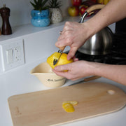 Hands using an Opinel | Essential Small Kitchen Knife Sets - Primo peeler to zest a lemon over a ceramic juicer, with zest pieces on a cutting board.