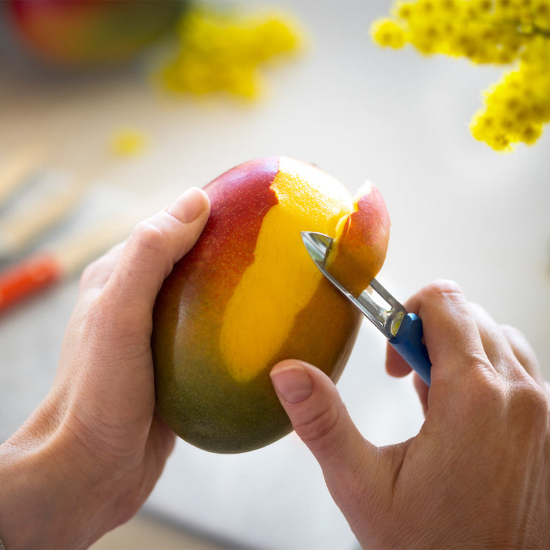 Close-up of a mango being peeled with the stationary peeler from the Opinel | Essential Small Kitchen Knife Sets, Fifties, showcasing its versatile kitchen utility.