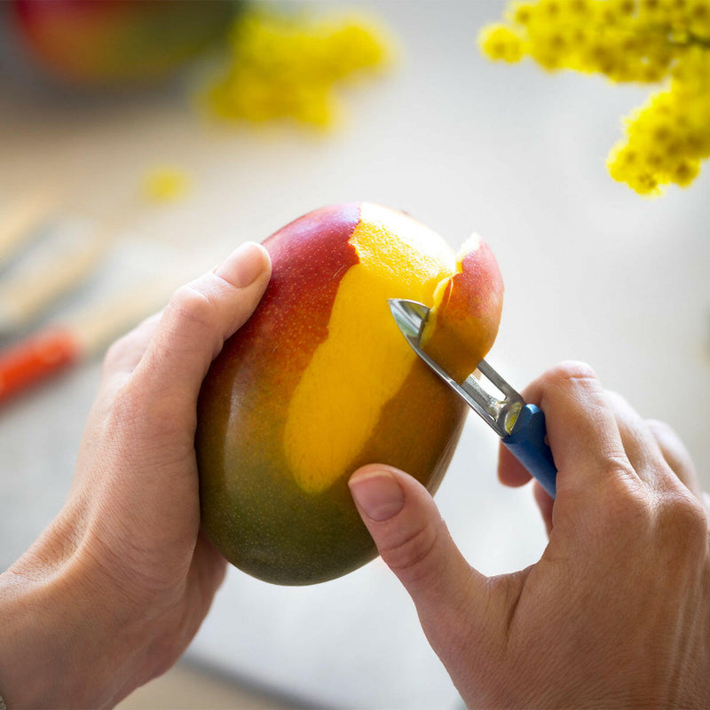 Hands using a Y-shaped peeler from the Opinel | Essential Small Kitchen Knife Sets - Primo to peel a mango, showcasing its versatility for home cooks.