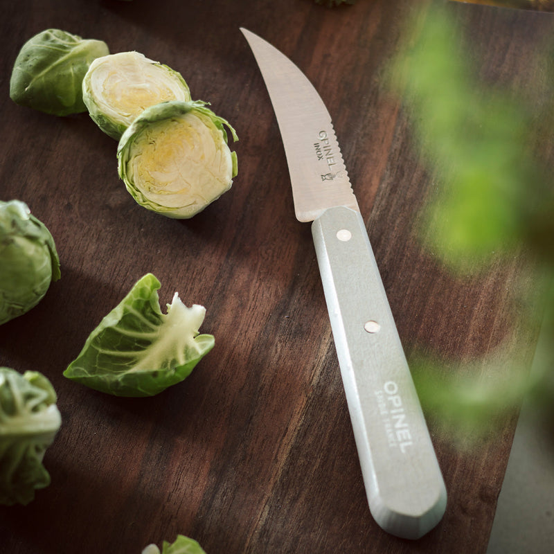 Opinel | Essential Small Kitchen Knife Sets, Primo, featuring a serrated paring knife on a wooden board with Brussels sprouts, ideal for versatile kitchen tasks.