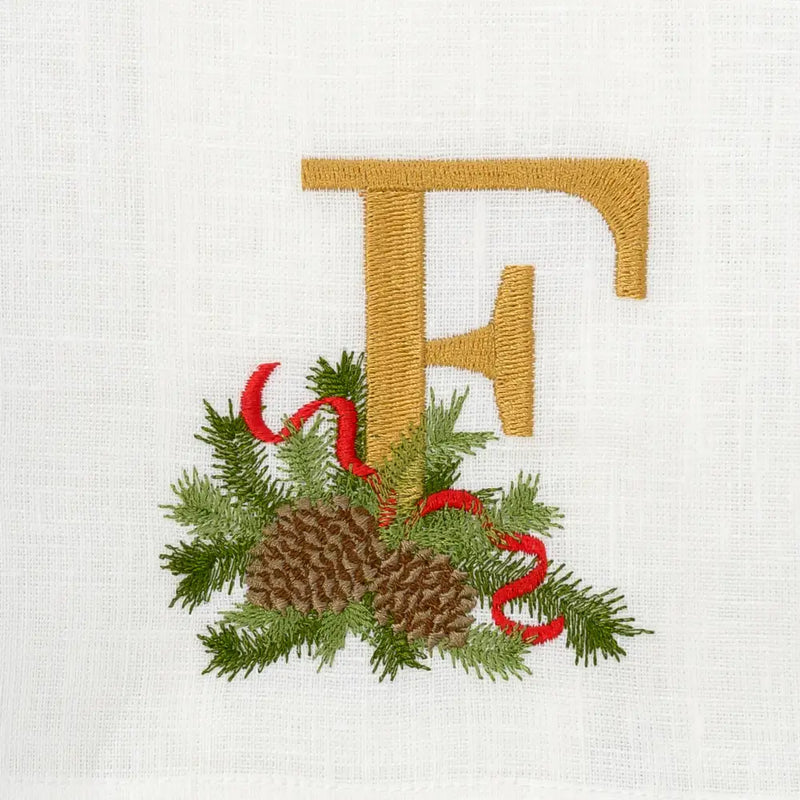 Winter Pine Monogram Towel, F, features a gold embroidered initial with pine cones, evergreen sprigs, and red ribbon accents, perfect for elegant kitchen or bathroom decor.