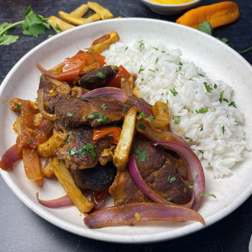 Vegan Peruvian Lomo Saltado featuring sautéed lion’s mane mushrooms, red onion, tomato, and French fries, served with white rice and cilantro.