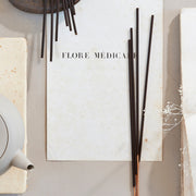 The Floral Society | SAMPLE Essential Oil Incense features black incense sticks on white paper, enhancing mood and meditation with therapeutic-grade essential oils.