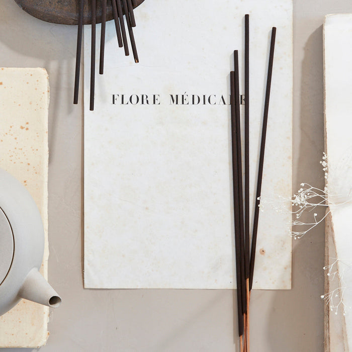The Floral Society | SAMPLE Essential Oil Incense features black incense sticks on white paper, enhancing mood and meditation with therapeutic-grade essential oils.