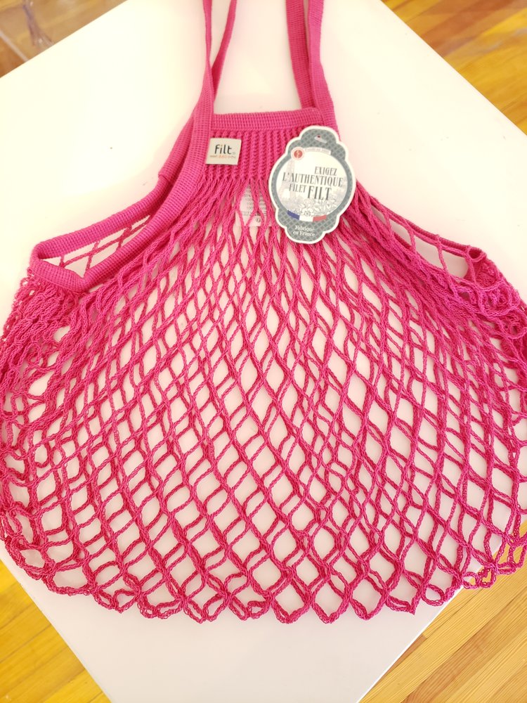 Filt | French Market Bags - Raspberry: A stylish, durable pink mesh shopping bag with a label, perfect for carrying groceries like wine and produce.