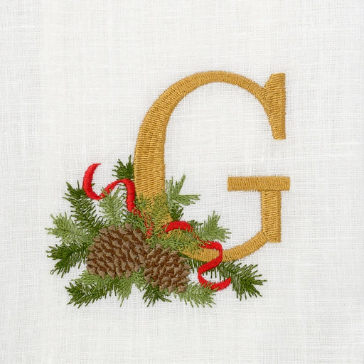 Winter Pine Monogram Towel by Arte Italica & Crown Linen Designs, featuring a gold 'G' with evergreen sprigs and pine cones on white linen.