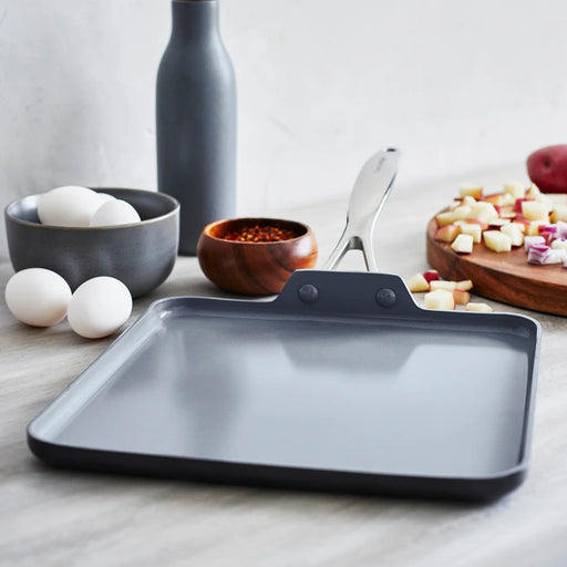 GreenPan Valencia Pro Ceramic Nonstick 11 Square Griddle on a countertop, surrounded by eggs, spices, diced potatoes, and a gray bottle, ready for cooking.