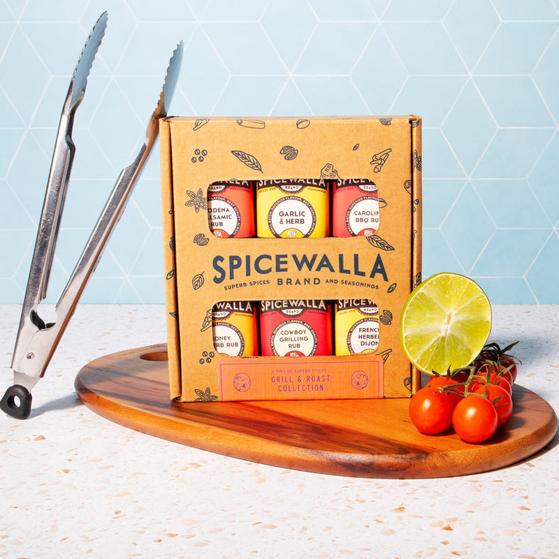 Spicewalla | Grill & Roast Gift Collection, Grill & Roast 6 Pack, featuring six spice jars on a cutting board with grilling tongs, lime, and cherry tomatoes.