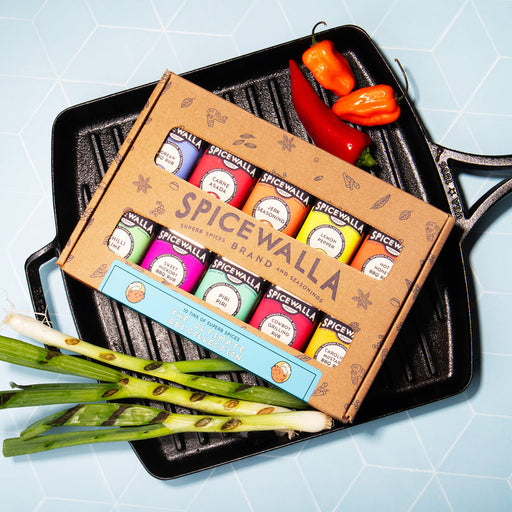 Spicewalla | Ultimate Backyard BBQ Collection, 10 Pack, in a grill pan with mini spice tins labeled for various BBQ blends, surrounded by chile peppers and scallions.
