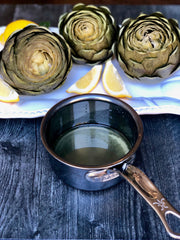 Hestan NanoBond | Cookware, .75qt Butter Warmer Pan, showcased with artichokes and lemon wedges, on a white platter, emphasizing its ergonomic design and durability.