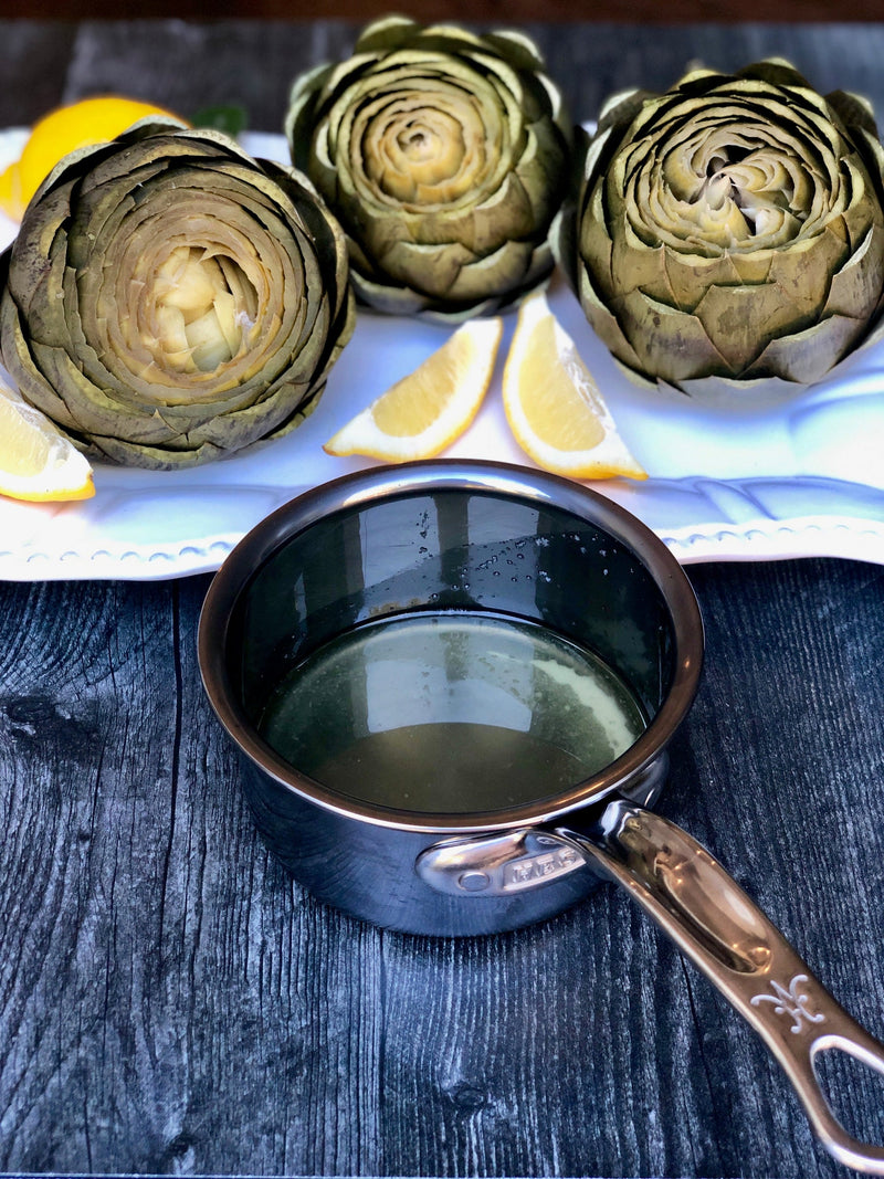 Hestan NanoBond | Cookware, .75qt Butter Warmer Pan, showcased with artichokes and lemon wedges, on a white platter, emphasizing its ergonomic design and durability.