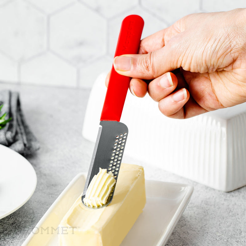 Hand holding Microplane Butter Blade, red handle, perforated blade creating decorative butter curl on white dish, showcasing efficient design for easy butter use.