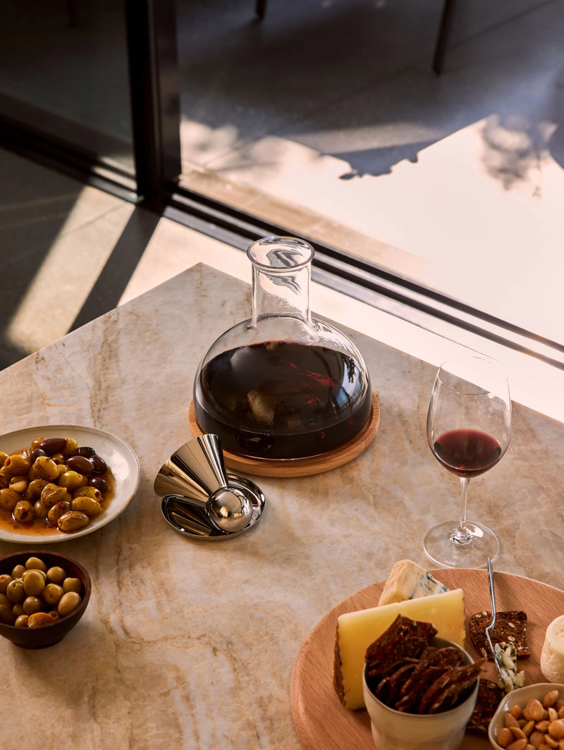 Holcomb Studio Puddle Coasters, Set of Four, on a table with wine and snacks, showcasing their elegant stainless steel design and functional, protective features.