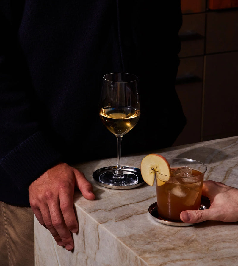 Holcomb Studio Puddle Coasters, Set of Four displayed with a glass of wine, showcasing their elegant and functional design for protecting surfaces from condensation.